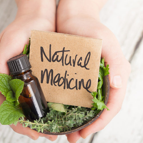 Bowl of herbs and essential oil and card saying Natural Medicine on light floor boards